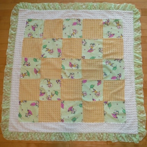 May include: A green and yellow patchwork baby quilt with a white ruffled border. The quilt is made of squares with a checkered pattern and squares with a floral pattern featuring small fairies.