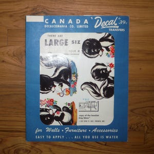 May include: A vintage Canada Decalcomania Co. Limited transfer sheet featuring black and white skunk illustrations with colourful floral accents. The blue packaging includes the text "LARGE SIZE", "Decal", and "for Walls, Furniture, Accessories".