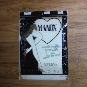 May include: A package of Manon brand nylons in a clear plastic sleeve. The packaging features a black and white graphic of legs, a heart shape, and the text "MANON" and "NYLONS." A vertical scale on the right side lists numbers from 28 to 35.