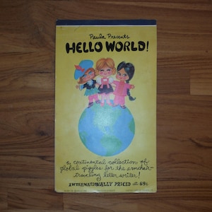 May include: A rectangular yellow booklet titled Paula Presents HELLO WORLD! featuring an illustration of three children standing on a globe. The text reads a continental collection of global giggles for the armchair-traveling letter writer!