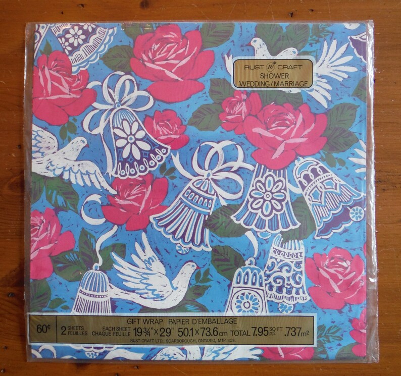 May include: A blue and white gift wrap with pink roses and white doves. The paper is designed for showers and weddings. The text on the paper reads "Rust & Craft Shower Wedding/Marriage 60 2 Sheets Each Sheet 19 3/4" x 29" 50.1 x 73.6 cm Total 7.95 sq ft .737 m&sup2; Rust Craft Ltd. Scarborough, Ontario, M1P 3C4"