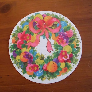 Peut inclure: Une assiette en papier ronde avec un motif de couronne color&eacute;. La couronne est faite de feuilles vertes, de fleurs roses et de baies rouges. Un n&oelig;ud rose est au centre de la couronne.