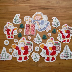 Könnte beinhalten: Eine Sammlung gestickter Weihnachtsdekorationen, darunter Weihnachtsmänner in roten Anzügen, Weihnachtsbäume, ein Engel und Geschenkboxen. Die Dekorationen sind in verschiedenen Formen und Größen mit weißem Rand.