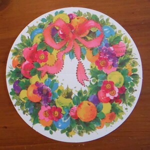 Peut inclure: Une assiette en papier ronde avec un motif de couronne color&eacute;. La couronne est compos&eacute;e de feuilles vertes, de baies rouges et jaunes et d'un n&oelig;ud rose. La couronne est entour&eacute;e d'un fond blanc.