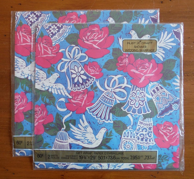 May include: Two sheets of blue gift wrap with a white dove, pink roses, and white bells. The text on the wrap reads "Rust & Craft Shower Wedding/Marriage" and "Gift Wrap Papier d'Emballage 19 3/4" x 29" 50.1 x 73.6 cm Total 7.95 sq ft .737 m&sup2;".