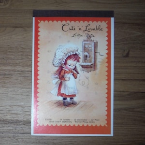 May include: A notepad with a vintage illustration. The cover features a drawing of a young girl in a bonnet and apron, with the text "Cute 'n Lovable Letter Notes." The notepad has a red border with a scalloped edge and a brown top.