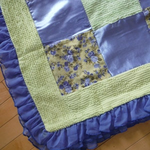 May include: A green and blue patchwork quilt with a ruffled edge. The quilt is made of different fabrics, including satin and floral print.