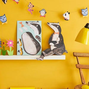 Puede incluir: Una habitaci&oacute;n con paredes amarillas brillantes con una guirnalda de caras de animales. Una ilustraci&oacute;n de tej&oacute;n est&aacute; en un estante con un libro, un &aacute;baco y una silla de madera con una l&aacute;mpara amarilla. Tambi&eacute;n se exhiben un peluche colorido y un p&oacute;ster.