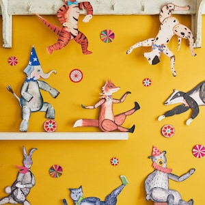 Puede incluir: Una exhibici&oacute;n caprichosa de recortes de animales de papel, incluyendo un tigre, un elefante, un zorro y un oso, contra un fondo amarillo. Cada animal est&aacute; adornado con sombreros de fiesta y accesorios. Decoraciones coloridas de estrellas salpicadas.