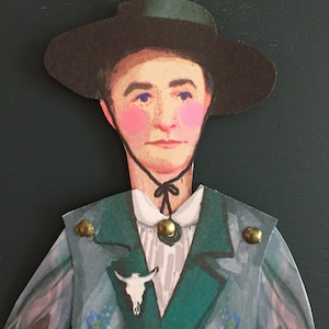 May include: A paper doll cutout of a person wearing a wide-brimmed black hat, a green jacket with gold buttons, a white shirt with a black bow tie, and a skull pin. The jacket is decorated with blue forget-me-not flowers.