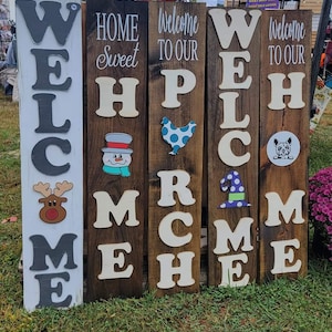 May include: Five wooden signs with white lettering spelling out "Welcome", "Home Sweet Home", "Welcome to Our Home", "Welcome", and "Welcome to Our Home". Each sign has a different seasonal or holiday-themed image on it, including a snowman, a chicken, a witch's hat, a reindeer, and a dog.