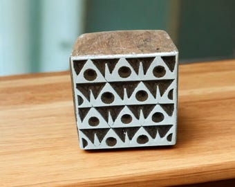 Peut inclure: Un bloc de bois avec un motif géométrique de triangles et de cercles. Le bloc est peint en blanc et marron. Le motif est répété sur la surface, créant un motif symétrique. Cet objet est probablement utilisé pour l'impression ou le tamponnage.