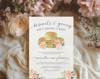 May include: Baby shower invitation with the text "biscuits & gravy SHE'S HAVING A BABY!". The invitation features an illustration of biscuits and flowers in shades of peach and green. The invitation is surrounded by flowers.