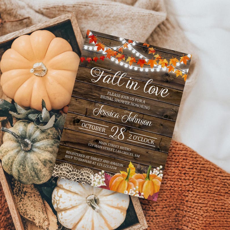 May include: A rustic wooden tray holds several pumpkins in shades of orange, green, and white. A fall-themed invitation with the text "Fall in love" and details for a bridal shower is also present.