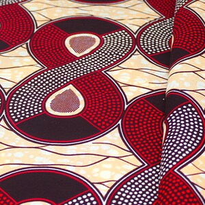 Può includere: Primo piano di un tessuto fantasia con un motivo ripetuto. Il motivo presenta grandi forme stilizzate in rosso, nero e bianco su uno sfondo beige. Le forme sono delineate in rosso e riempite di punti.