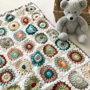 May include: A crocheted blanket with a white background and colorful circular motifs in shades of green, blue, orange, and brown. The blanket is made with a textured stitch and has a scalloped edge.