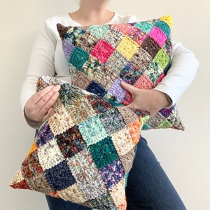 May include: Two crocheted cushion covers with a patchwork design. The larger cushion cover is made with bright colours, including pink, yellow, green, and purple. The smaller cushion cover is made with more muted colours, including brown, beige, and teal.
