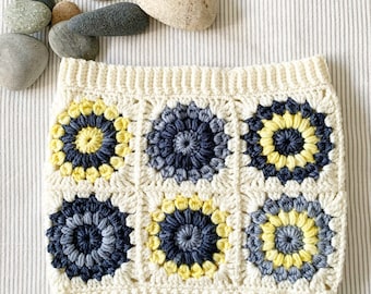 May include: A crocheted headband with a white background and a pattern of yellow and grey flowers.