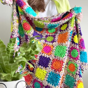 May include: A vibrant, handmade crochet blanket featuring a patchwork design of colorful squares. The blanket showcases a spectrum of bright hues, including pink, green, orange, purple, and yellow, creating a cheerful and cozy aesthetic. The blanket is a perfect home decor item.