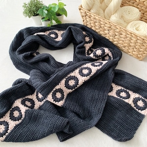 以下が含まれることがあります： 白とベージュの縁取りが施された黒いクロシェのストール。花柄が繰り返しデザインされています。