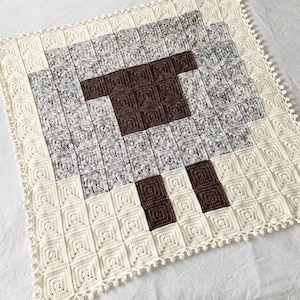 May include: A crocheted baby blanket with a brown sheep design. The blanket is white with a crocheted border.