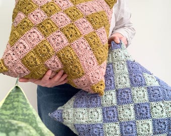 May include: Two crocheted throw pillows with a checkered pattern. One pillow is pink and mustard yellow, the other is light blue and green.