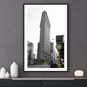 Puede incluir: Fotografía en blanco y negro del Flatiron Building en la ciudad de Nueva York con un reloj amarillo en primer plano.