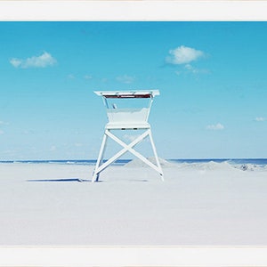May include: A white lifeguard stand on a sandy beach with a blue sky and white clouds in the background.