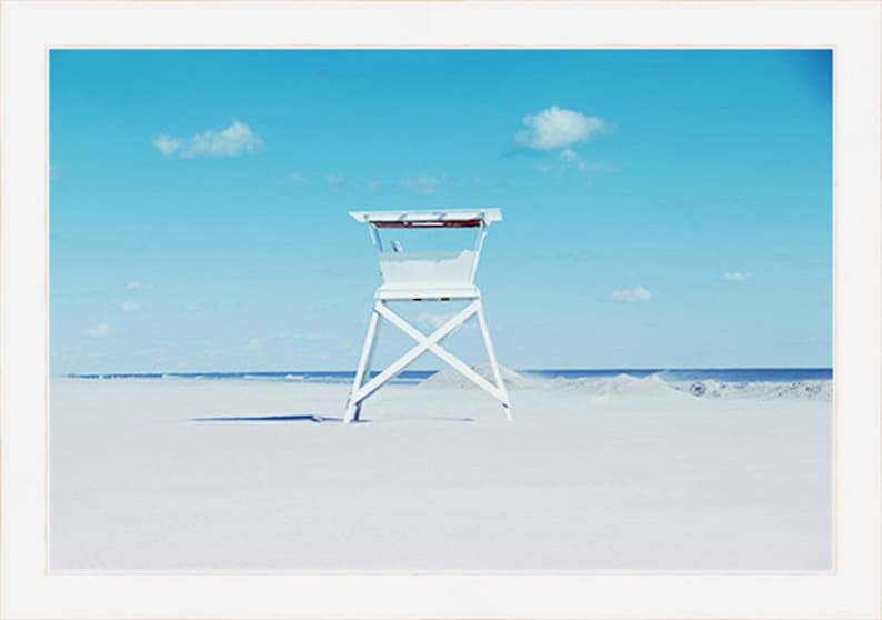 May include: A white lifeguard stand on a sandy beach with a blue sky and white clouds in the background.
