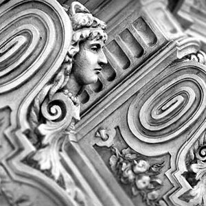 May include: Black and white photograph of a detailed, ornate, architectural design with a spiral pattern. The design features a sculpted human face with a crown.