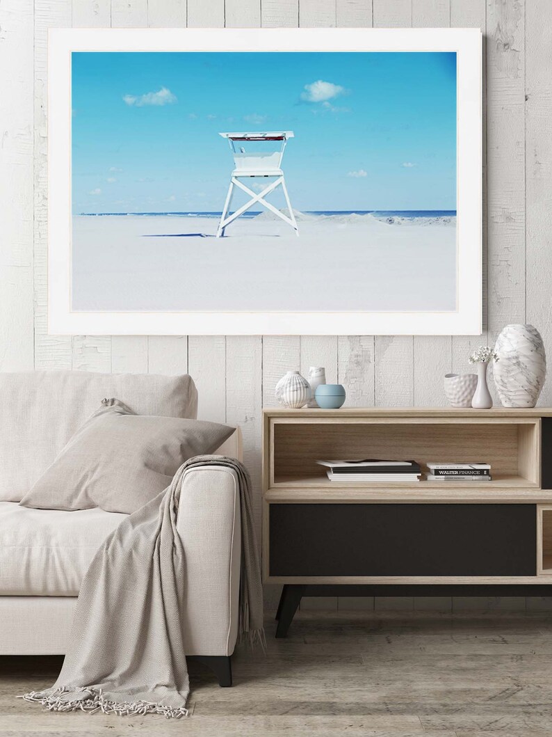 May include: A white lifeguard stand on a white sandy beach with a blue sky and white clouds in the background.