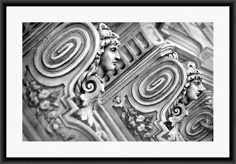 May include: Black and white photograph of a close-up of an ornate architectural detail with a spiral design and two sculpted faces.