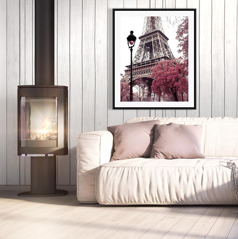 May include: A white couch with two pink throw pillows in front of a fireplace and a framed print of the Eiffel Tower with pink trees in the foreground.