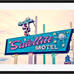 May include: A vintage neon sign for a motel called "Satellite Motel". The sign is blue with pink lettering and features a stylized satellite with stars around it.