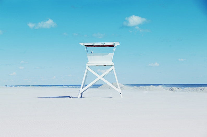 May include: A white lifeguard stand on a sandy beach with a blue sky and white clouds in the background.