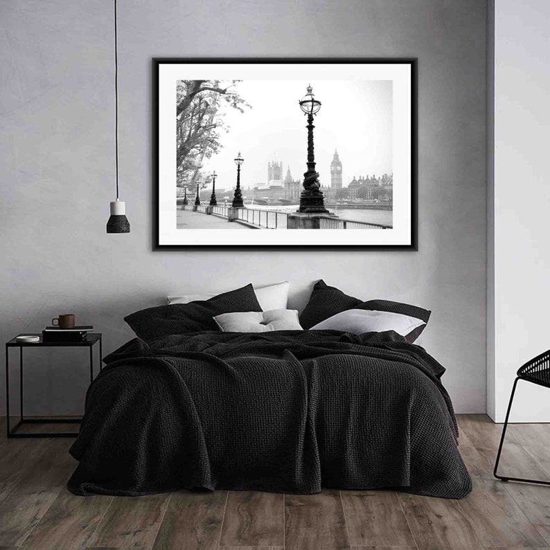 May include: Black and white photograph of the Houses of Parliament in London, England. The photo is framed and hanging on a wall above a black bed with white pillows.