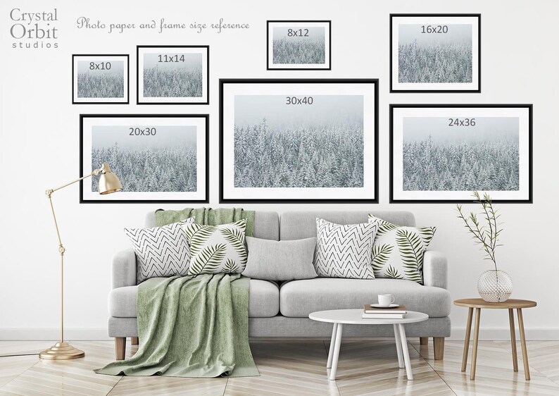 May include: A white wall with a couch and two end tables. There are eight framed pictures of a snowy forest scene hanging on the wall. The pictures are labeled with their dimensions in inches, such as 8x10, 11x14, 20x30, 30x40, 24x36, 8x12, and 16x20.