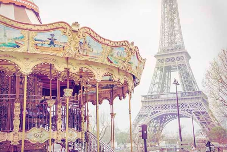 Op de afbeelding: Een vintage carrousel met sierlijke details staat voor de Eiffeltoren in Parijs, Frankrijk. De carrousel is geschilderd in pastelkleuren en heeft een gouden rand. De Eiffeltoren is een metalen constructie met een lichtgrijze afwerking.