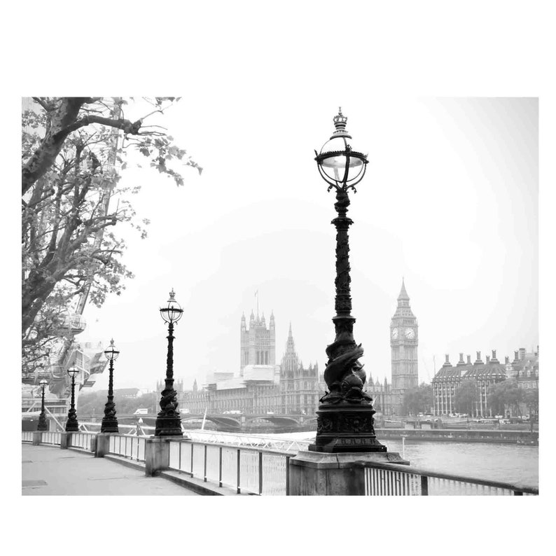 May include: A black and white photo of a street scene in London, England. The photo shows a row of lampposts with ornate designs, and in the background, the Houses of Parliament and Big Ben can be seen.