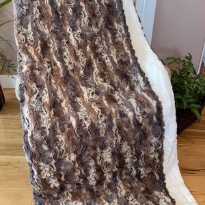 May include: A soft, plush throw blanket with a brown and white striped pattern. The blanket is reversible, with a white faux fur side and a brown and white striped side.