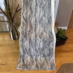 May include: A soft, gray and white faux fur throw blanket with a wavy pattern. The blanket is draped over a chair.