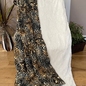 May include: A reversible throw blanket with a black, brown and tan animal print on one side and a white, fluffy texture on the other side.