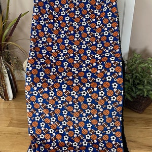 May include: A blue fleece blanket with a pattern of various sports balls, including basketballs, footballs, and soccer balls. The blanket has a black sherpa backing.