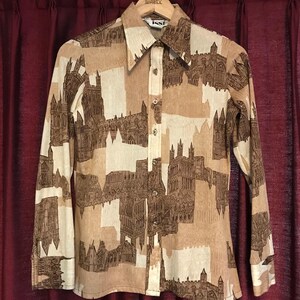 May include: A long-sleeved button-down shirt with a repeating pattern of brown and beige architectural designs. The shirt has a pointed collar and is hanging on a wooden hanger. The brand name "ISSI" is visible on the label.