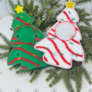 May include: Two Christmas tree-shaped felt ornaments. One is green with red stripes and a yellow star, the other is white with red stripes and a yellow star. Both have a circular opening in the center.