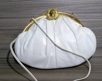May include: A white, textured, crescent-shaped handbag featuring a gold-toned metal frame with a lion head clasp at the centre. The bag has a thin, matching white shoulder strap and a gathered, pleated design that creates a soft, rounded silhouette.