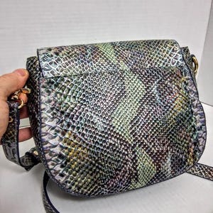 May include: A crossbody bag featuring a textured snakeskin pattern in iridescent shades of green, blue, purple, and silver. The bag has a rounded flap closure, gold-toned metal hardware attachments for the strap, and a matching adjustable shoulder strap.