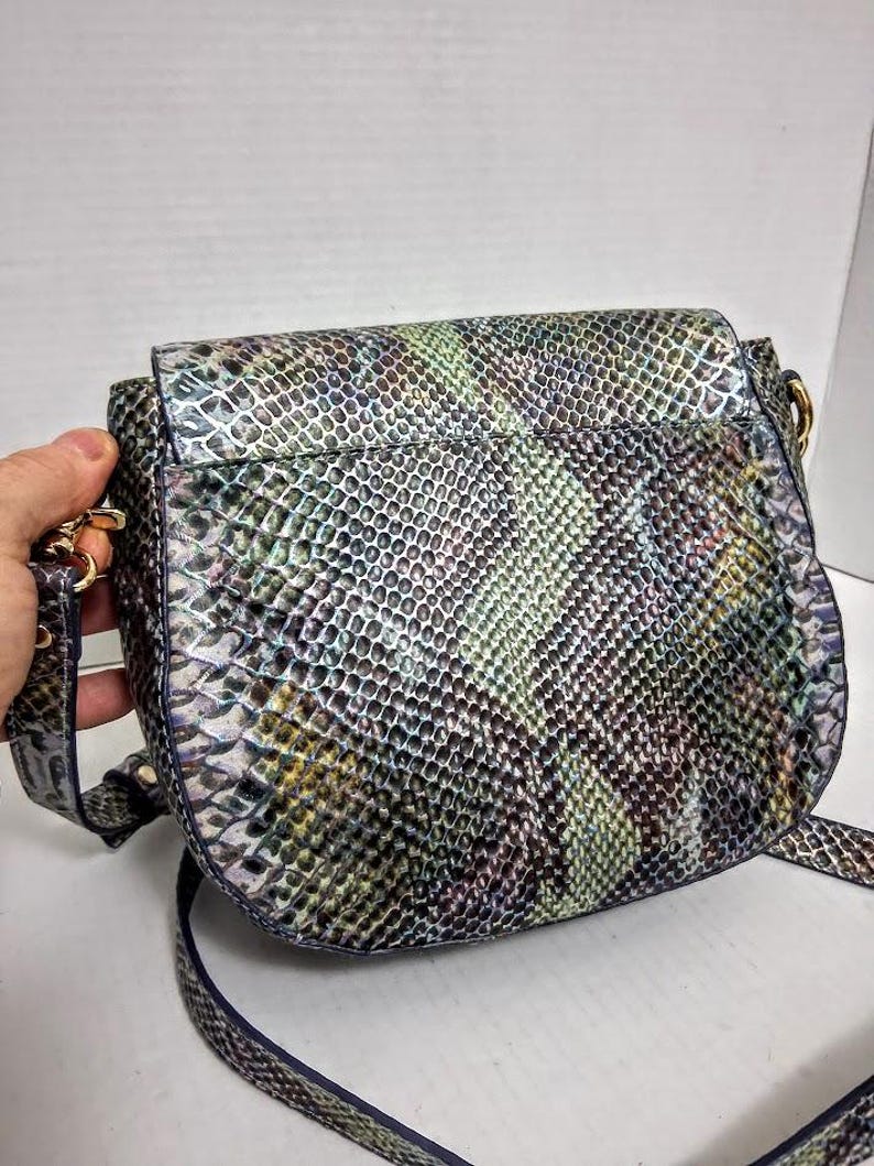 May include: A crossbody bag featuring a textured snakeskin pattern in iridescent shades of green, blue, purple, and silver. The bag has a rounded flap closure, gold-toned metal hardware attachments for the strap, and a matching adjustable shoulder strap.