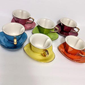 May include: A set of six heart-shaped teacups and saucers in assorted colors including blue, magenta, green, dark red, yellow, and orange. Each cup features a white interior, a gold-toned handle, and a matching colored exterior finish.