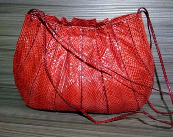 May include: A bright red handbag featuring a textured snakeskin pattern with a glossy finish. The bag has a rounded, pleated body design with a gathered top opening and thin, matching red shoulder straps attached to the sides of the structure.